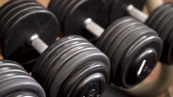 Closeup slow slider shot to the left looking down on row of dumbbells on a rack. alt