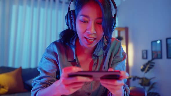 Asia girl gamer competition play video game online with smartphone colorful neon lights.