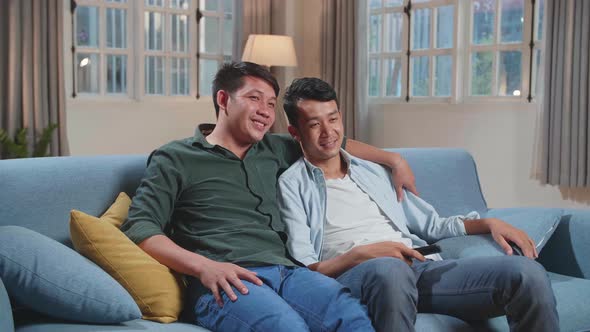Happy Asian Gay Couple Watching Tv While Sitting On A Couch In Apartment, Watching Funny Videos alt
