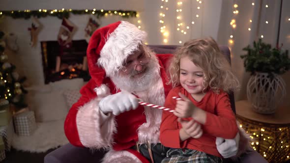Funny Santa Claus Sitting on His Rocker with Little Cute Boy with Christmas Lollipop Sitting on His