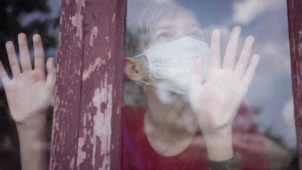 Boy in Mask Inside Looks at the Window and Takes Off the Mask alt