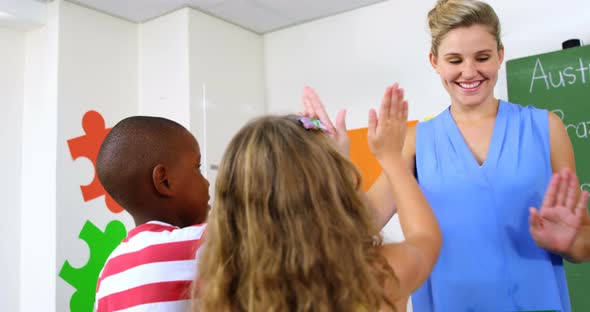 School teacher giving high five to school kids in classroom alt