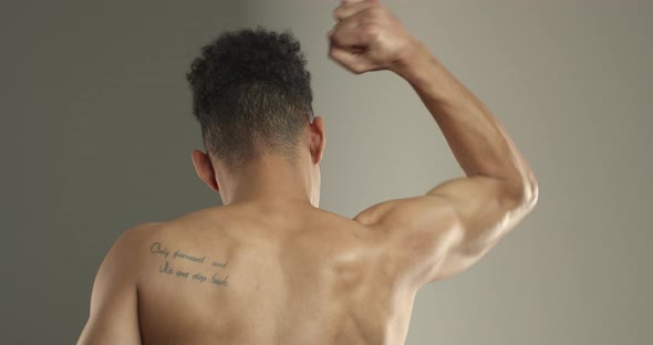 Closeup Rear View of Darkskinned Sportsman Flexing Biceps on Right Arm alt