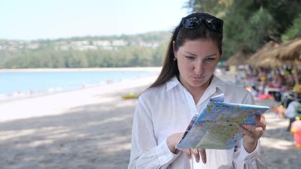 Young Woman in a White Shirt on the Beach Considers a Map alt