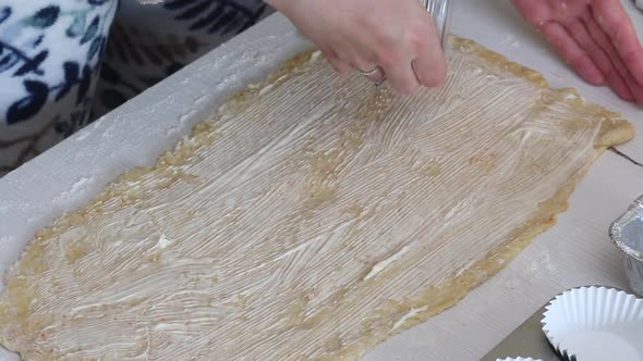 A Woman Sprinkles Stuffing Onto Rolled Out Dough For Kruffin. alt