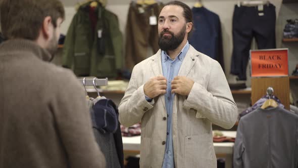Handsome Bearded Caucasian Man Trying on Jacket in Shop and Friend Approving His Choice. Confident alt