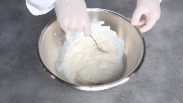 Сhef kneads the dough in a bowl with his gloved hands