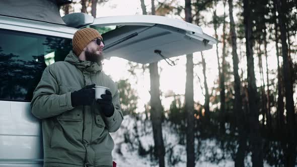 Man Drinks Leaning on the Back of a Van with Pop Up Roof in the Woods in Winter