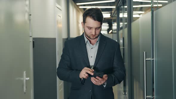 Young Businessman Uses a Mobile Phone to Work in the Office Corridor alt