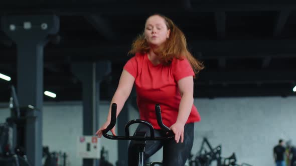 Athletic Woman Riding on Spinning Stationary Bike Training Routine in Gym Weight Loss Indoors alt