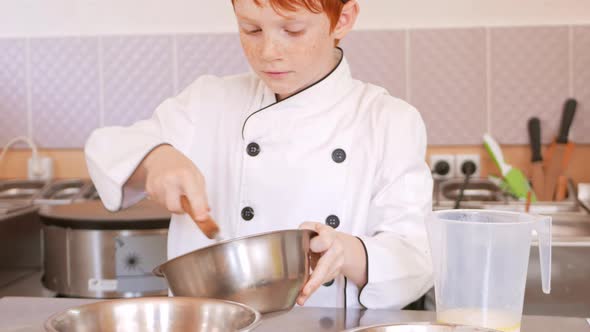 Redhaired Boy in Chef's Costume Cooks Pancakes in Kitchen Kneads Dough Assistant Makes Breakfast
