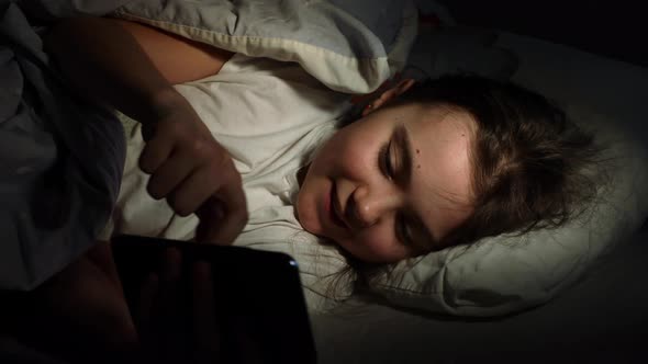 Little Girl Looking at The Smartphone And Then Hides Under The Blanket