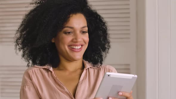 Cute African American Woman Browses Content or Communicates on Social Networks Using Digital Tablet alt