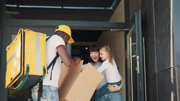 The Courier Carries the Parcel to the Little Girl and Her Mother at the Door alt