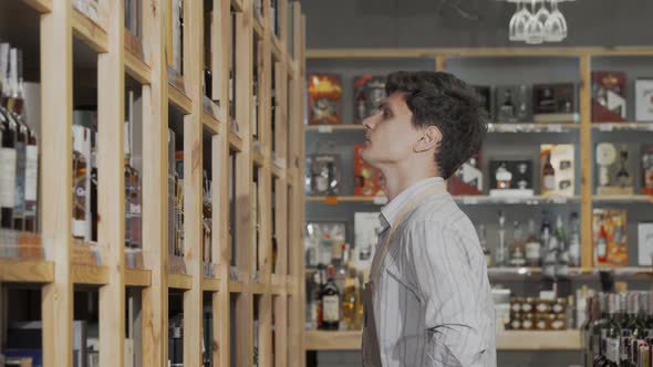 Young Male Winemaker Organizing Bottles on Sale on the Shelves at His Store