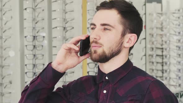 Cheerful Young Man Talking on the Phone at the Optician Store alt