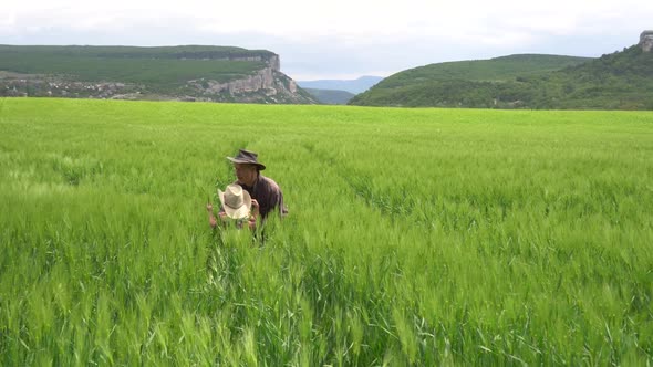 A Farmer Father with Happy Small Daughter Inspects a Green Wheat Field in Spring alt