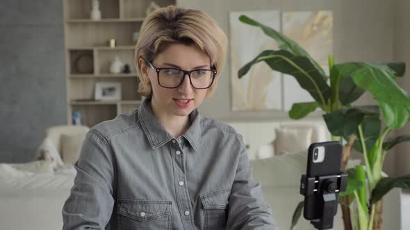 Blonde Blogger in Glasses Talks Sitting at Black Smartphone alt