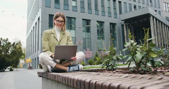 Confident Young Woman Working Outdoors Sitting Near Office Building Typing on Laptop alt