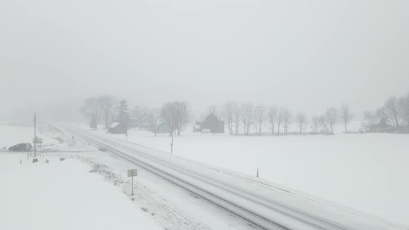 Snow filled sky over rural farm on edge of highway. Vehicle turning at intersection.