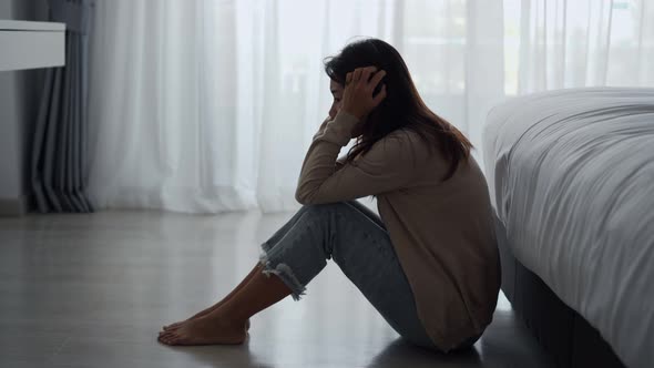 Lonely young woman feeling depressed and stressed sitting in the dark bedroom