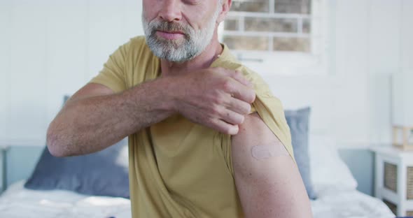 Happy caucasian mature man showing plaster on arm where he was vaccinated against coronavirus alt