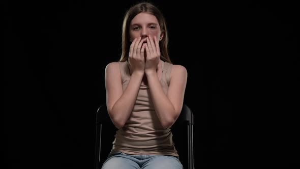 Front View Scared Teenage Girl Showing Bruised Face Looking at Camera Sitting on Chair alt