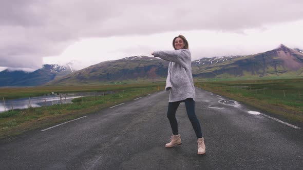 Happy Young Woman Dancing on Asphalt Road in Iceland and Having Some Fun Slow Motion alt