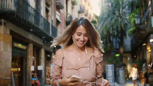 Happy Woman Walking in Earphones in Slow Motion. Cute Girl Flirting Outdoor. alt