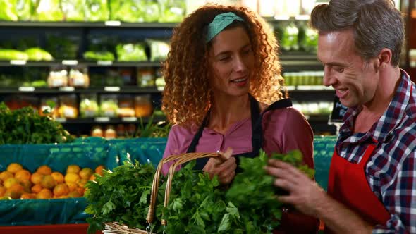 Smiling staff checking leafy vegetables in organic section alt
