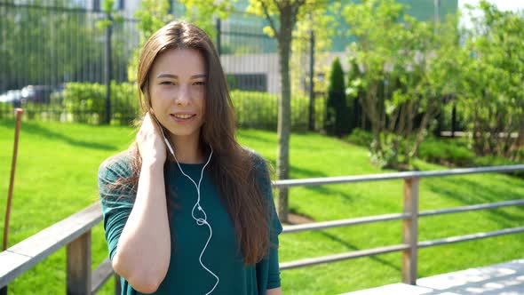 Young Woman Listening the Music By Headphones. Attractive Female with Cute Smile with Mobile Phone