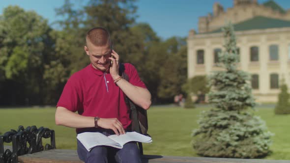 Busy Male Student Answering Phone Sitting on Bench alt