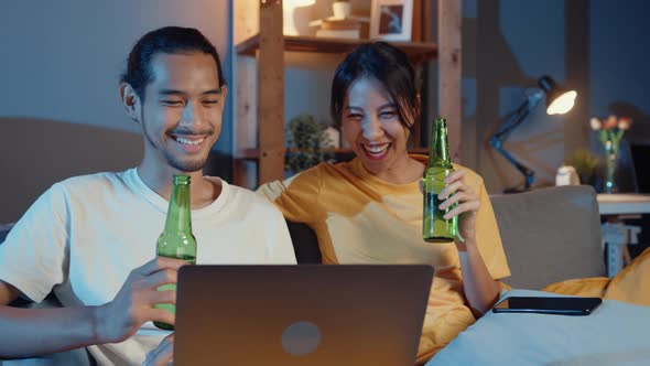 Happy young asian couple enjoy night party event online sit couch use laptop computer video call.