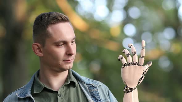 Young Man Looks on His Robotic Hand