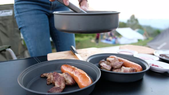 Closeup of a woman cooking steak and grilled sausages while camping outdoors