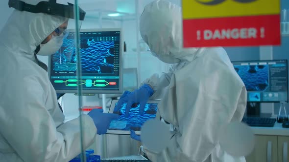 Chemists in Coverall Trying To Develop Vaccine Using Tablet Standing Behind the Glass Wall alt
