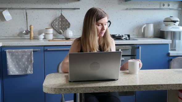 Business Woman in Black Dress Having Coffee and Working with Laptop in the Kitchen