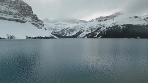 Drone flies between the trees and shows view of the Bow Lake and snowy mountains in Alberta, Canada alt