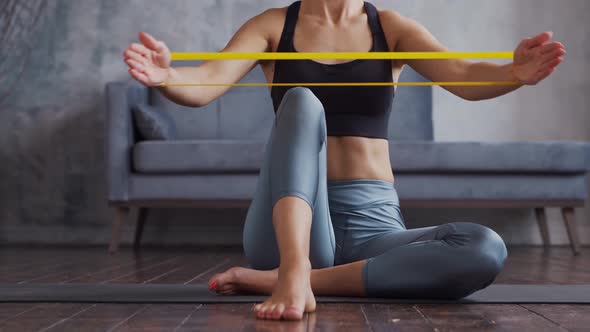 Young and sporty girl in sportswear is doing exercises in home interior using resistance band. alt