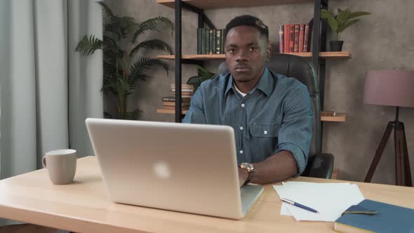African Man Employee Works in the Office at the Computer. Black Businessman Looking at Laptop Screen alt