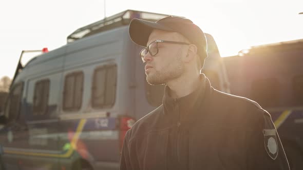 A Man in a Police Uniform is Standing Near Two Police Buses and Inspecting the Area alt