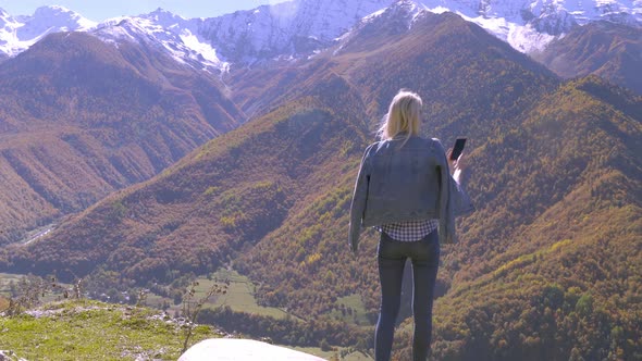 beautiful blonde takes photos or videos of a landscape in the autumn mountains. alt