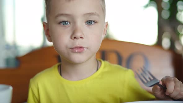 Child Dressed in a Yellow T-shirt Eats a Pancake in the Morning for Breakfast in a Cafe alt