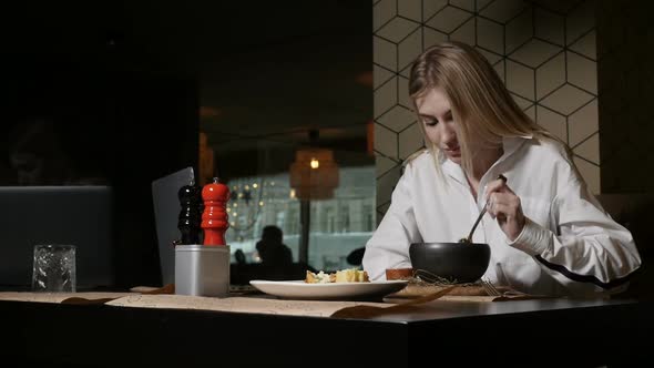 a Young Blonde Woman Eating Soup Sitting in a Restaurant alt