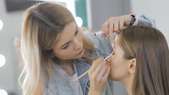 Professional Makeup Artist Doing Makeup on Eyes for Young Model in Beauty Salon