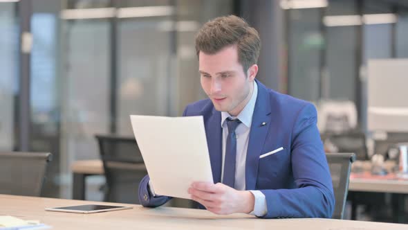 Businessman Celebrating Success While Reading Documents in Office alt