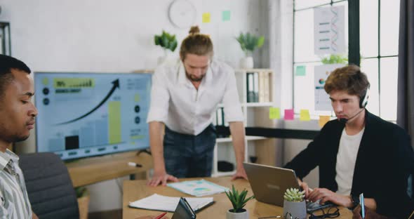 Male Business Leader in Modern Office, Looking at Camera. Busy Diverse Team Working in background alt
