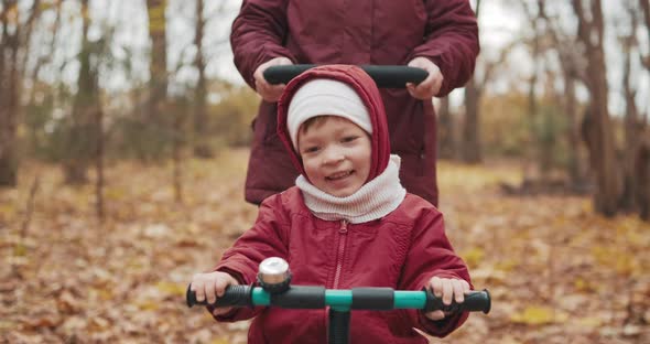 Mom Rides Cute Little Girl on Bicycle in Autumn Park