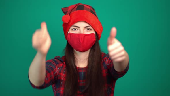 Portrait of Pretty Woman Wearing Christmas Red Hat and Medical Protective Face Mask Showing Thumbs