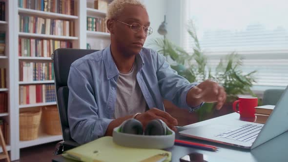 Handsome Darkskinned Man Listening to Music on Headphones and Typing on Laptop alt